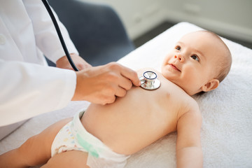 medicine, healthcare and pediatrics concept - close up of female doctor with stethoscope listening to baby girl's patient heartbeat or breath at clinic or hospital