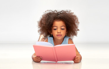 childhood, school and education concept - little african american girl reading book over grey backgr