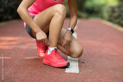 Photographie Female runner tying shoelace before running on park trail