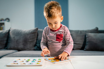 Small boy little playing at home alone by the table with puzzle developing mental skill having fun learning