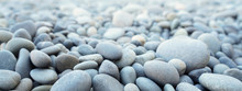 Round Stones On A Dry River Bed Outside In Nature. Smooth Pebbles With Light Gray Tones In Ambient Light.
