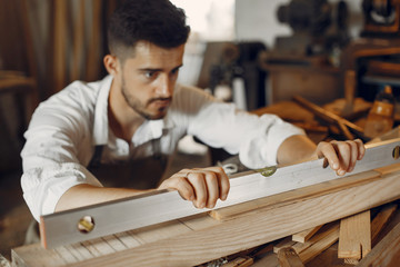 Wall Mural - Man working with a wood. Carpenter in a white shirt. Worker measures a board