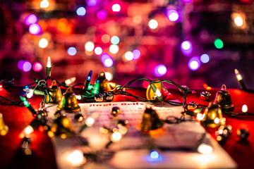 Jingle Bells Sheet Music lit by Christmas lights, surrounded by various bells.  Shallow depth of field with heavy bokeh.