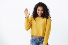 Shy Lovely African-american Girl In Yellow Sweater, Curly Hairstyle, Stooping As Raising Hand, Waving Hello, Hi Gesture, Smiling, Modest Woman Introduce Herself In Front Audience, White Background