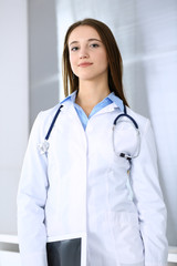 Wall Mural - Doctor woman happy and cheerful while standing in hospital office at highlight background. Medicine and healthcare concept