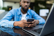 © F8  \ Suport Ukraine - Portrait of African guy talking on phone with laptop in front of him on table in cafe