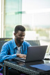 © F8  \ Suport Ukraine - African man sitting at table in cafe working with laptop and papers and drinking coffee