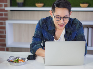 Wall Mural - Young Asian businessman working remotely from a home office with a laptop while sitting at the table