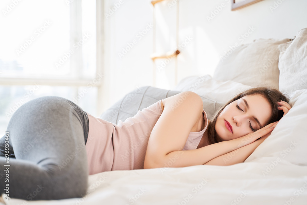 Photo of young woman sleeping lying on bed in bedroom - obrazy, fototapety, plakaty 