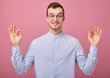 © Svitlana - Focus on his hands. A decent young man in a sky blue shirt and computer glasses stands on a pink background. Student, entrepreneur. Man points finger to the right, smiling. Happyness.