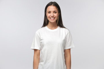 Portrait of smiling young woman in white t-shirt looking at camera, isolated on gray background