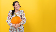 Happy Young Woman Holding A Pumpkin On A Yellow Background