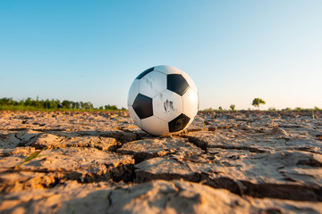 The football ball in a field that is dry and cracked in the evening sun