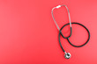 black stethoscope on a red background top view with copy space.