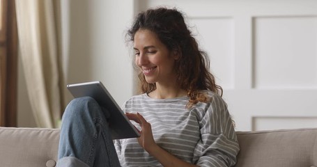 Happy young woman relaxing at home on sofa using tablet
