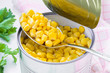 Spoon of canned sweet corn over a freshly opened tin can on a table. Side dish and ingredient for salads. Vegetarian