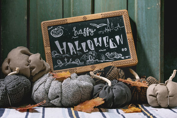 Wall Mural - Wool and textile pumpkins for Halloween holidays home decor with autumn leaves, black chalkboard with Happy Halloween lettering on knitted doormat with old wooden door at background.