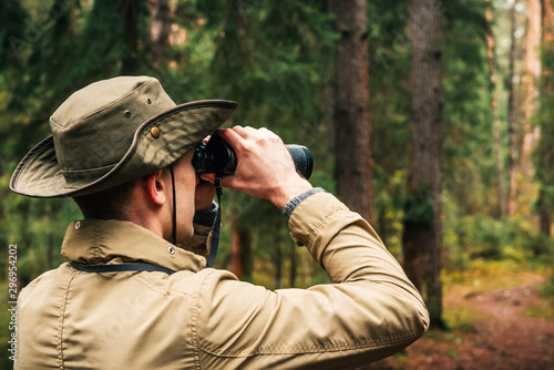 Fotomural A man in a hat and uniform green and beige holds binoculars and looks into the d