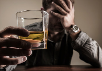 depressed and thoughtful alcoholic man on his 40s in front of whiskey glass wasted and stressed holding on temptation to drink in alcohol addiction and alcoholism problem