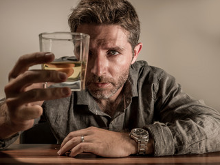 alcoholic depressed and wasted addict man sitting in front of whiskey glass trying holding on drinking in dramatic expression suffering alcoholism and alcohol addiction