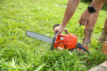 Wall Mural - hands of a man start an orange chainsaw.