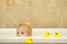 Little Adorable Baby Sitting In Bath Tub And Playing With Yellow Rubber Ducks