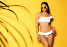 Beautiful Young Woman In White Bikini With Sunglasses On Yellow Background. Space For Text