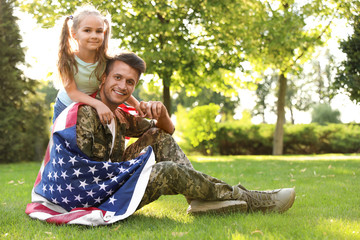 Wall Mural - Father in military uniform with American flag and his little daughter sitting on grass at park