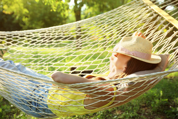 Poster - Young woman with hat resting in comfortable hammock at green garden