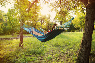 Poster - Young woman reading book in comfortable hammock at green garden