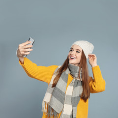 Canvas Print - Beautiful young woman in warm clothes  taking selfie on grey background. Winter season