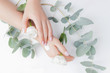 © Parilov - Woman applying hand cream flowers eucalyptus on white background, top view. Concept cosmetic body care, anti-wrinkles, anti-aging spa