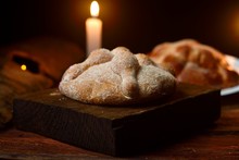 Mexican Tradition, Pan De Muerto Made With Butter And Egg, On A Square Wooden Base In Turn On Wooden Logs, Diffuse Background With A Lit Candle
