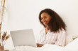 © Anatoliy Karlyuk - Indoor shot of happy cute young African American woman with curly hair watching favorite series via online platform sitting in cozy bedroom with generic laptop, looking at screen with broad smile