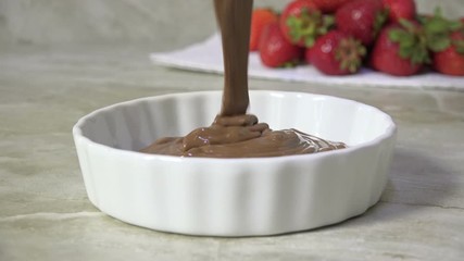 Wall Mural - Pouring melted milk chocolate into a dish by fresh strawberries slow motion