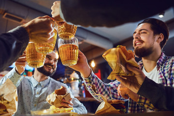 Wall Mural - Friends clink glasses with beer in a bar.