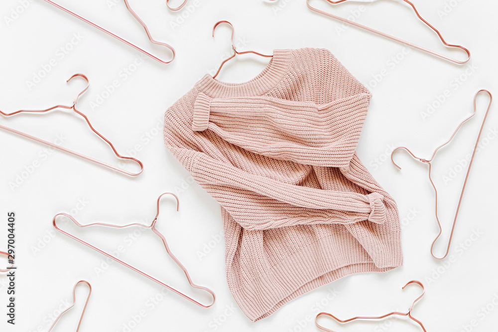 Pale pink knitted sweater with metallic hangers on white background. Autumn and winter clothes. Store, sale, fashion concept. - obrazy, fototapety, plakaty 