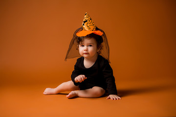 Wall Mural - baby in a witch costume for Halloween, child in a witch costume on an orange background isolate, space for text