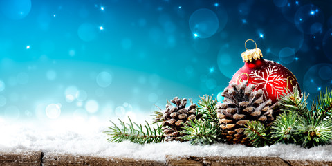 christmas - red ornament, pinecones and branches on snowy wooden table with blue bokeh background