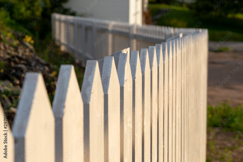 A long white picket fence with sun shining on the wood. There's a white ...