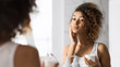 © Prostock-studio - Pretty Black Girl Applying Face Cream Standing In Bathroom, Panorama