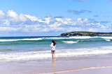 Fototapeta Konie - Young girl looking at the splashing wave on the beach of Playa de Somo İn Santander, Cantabria, Spain