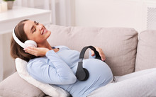 Peaceful Expectant Lady Listening To Music Lying On Couch Indoor