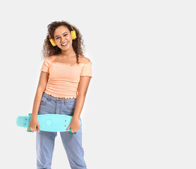 Poster - Beautiful African-American woman with skateboard listening to music on white background