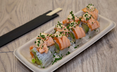 Japanese uramaki sushi. Bebi roll Rice rolls stuffed with tempura shrimp, avocado, chopped lettuce, crispy onion, flambéed salmon topin, anticuchera sauce and chives.