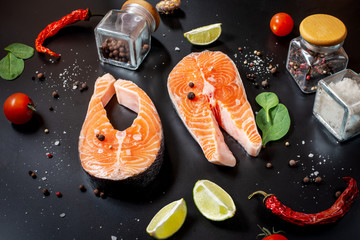 Two fresh raw salmon steaks with salt, peppers, lemon on stone background.