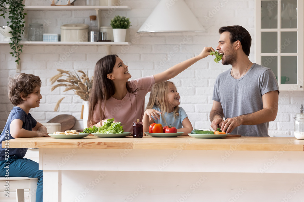 Happy family cooking salad together, smiling mother feeding father - obrazy, fototapety, plakaty 
