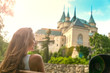 girl sits on a bench on a background of a beautiful castle.