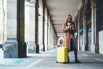 Tourist with suitcase holding smart mobile phone. Girl travels in Barcelona. Holiday concept in Spain street. Traveler hipster in glasses using internet technology in europe trip. Copy space mockup