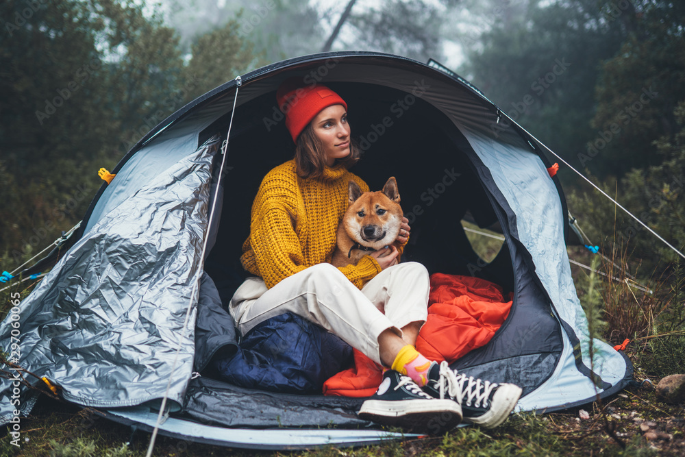 tourist traveler in camp tent hugging shiba inu on background foggy rain forest, person with puppy dog in mist nature trip, friendship love concept, happy girl resting dog together in campsite park - obrazy, fototapety, plakaty 